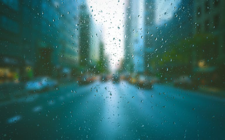 Blurred city scene through raindrop-covered window, creating a tranquil urban mood.